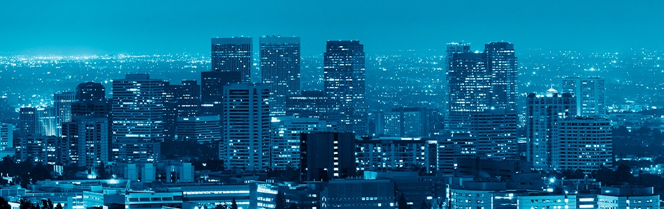 Imagem de uma vista aérea da cidade de Los Angeles à noite. A cidade está iluminada e os edifícios são mostrados em preto e branco. A imagem é sobre o conceito de cidades inteligentes, que são cidades que usam tecnologia para melhorar a qualidade de vida de seus habitantes.
