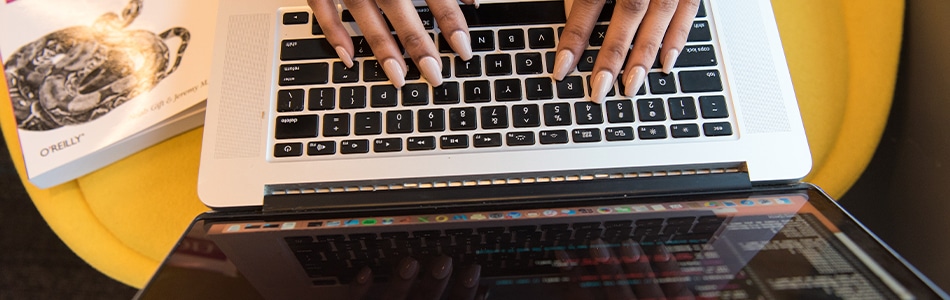 Uma foto de uma pessoa digitando em um MacBook Pro. A pessoa está sentada em uma mesa e está usando as teclas do MacBook Pro para digitar. A tela do MacBook Pro está mostrando um código de programação.
