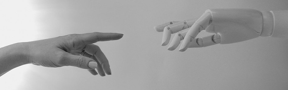 Imagem de duas mãos, uma humana e outra robótica. A mão humana é cinza e tem dedos longos e finos. A mão robótica é branca e tem dedos mais curtos e robustos. As duas mãos estão estendidas uma para a outra, como se estivessem se cumprimentando.