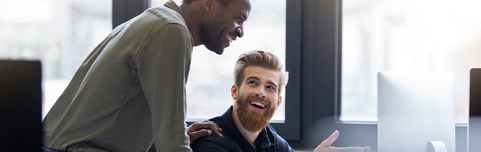 Imagem de dois homens rindo um do outro enquanto trabalhavam em um computador.