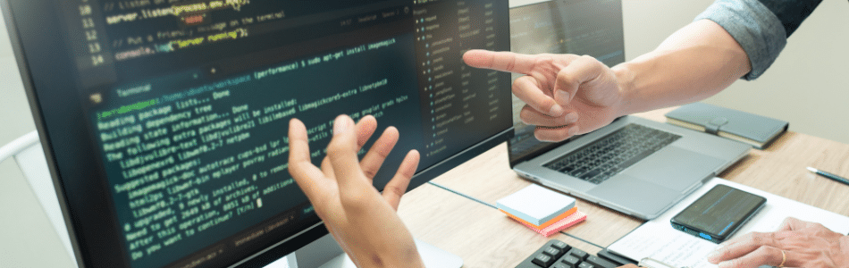 Descrição de Imagem: Mãos apontando para uma tela de computador com códigos de desenvolvimento.