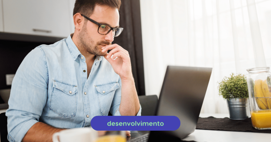 Um homem de óculos e camisa jeans azul claro está sentado à mesa, trabalhando em um laptop na cozinha ou na área de jantar. Uma xícara e uma pequena planta estão sobre a mesa. A palavra “desenvolvimento” aparece na imagem, talvez sugerindo seu trabalho envolvendo boas práticas de documentações de API.