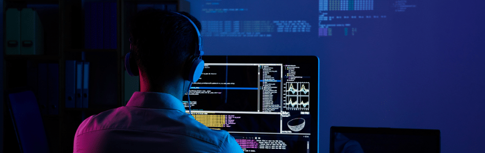 Uma pessoa usando fones de ouvido e camisa branca está trabalhando em um computador em uma sala mal iluminada. Várias telas exibem linhas de código e gráficos, indicando que estão envolvidos na codificação, análise de dados ou realização de testes de API.